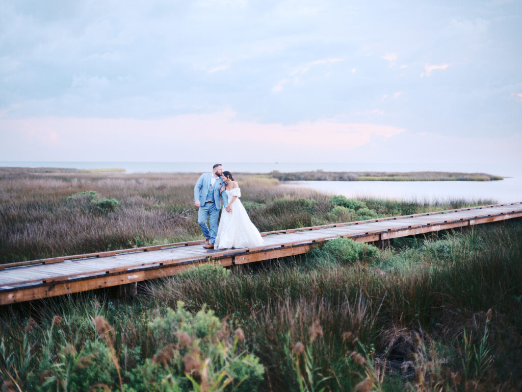 a bride and groom standing on a wooden bridge in the Outerbanks