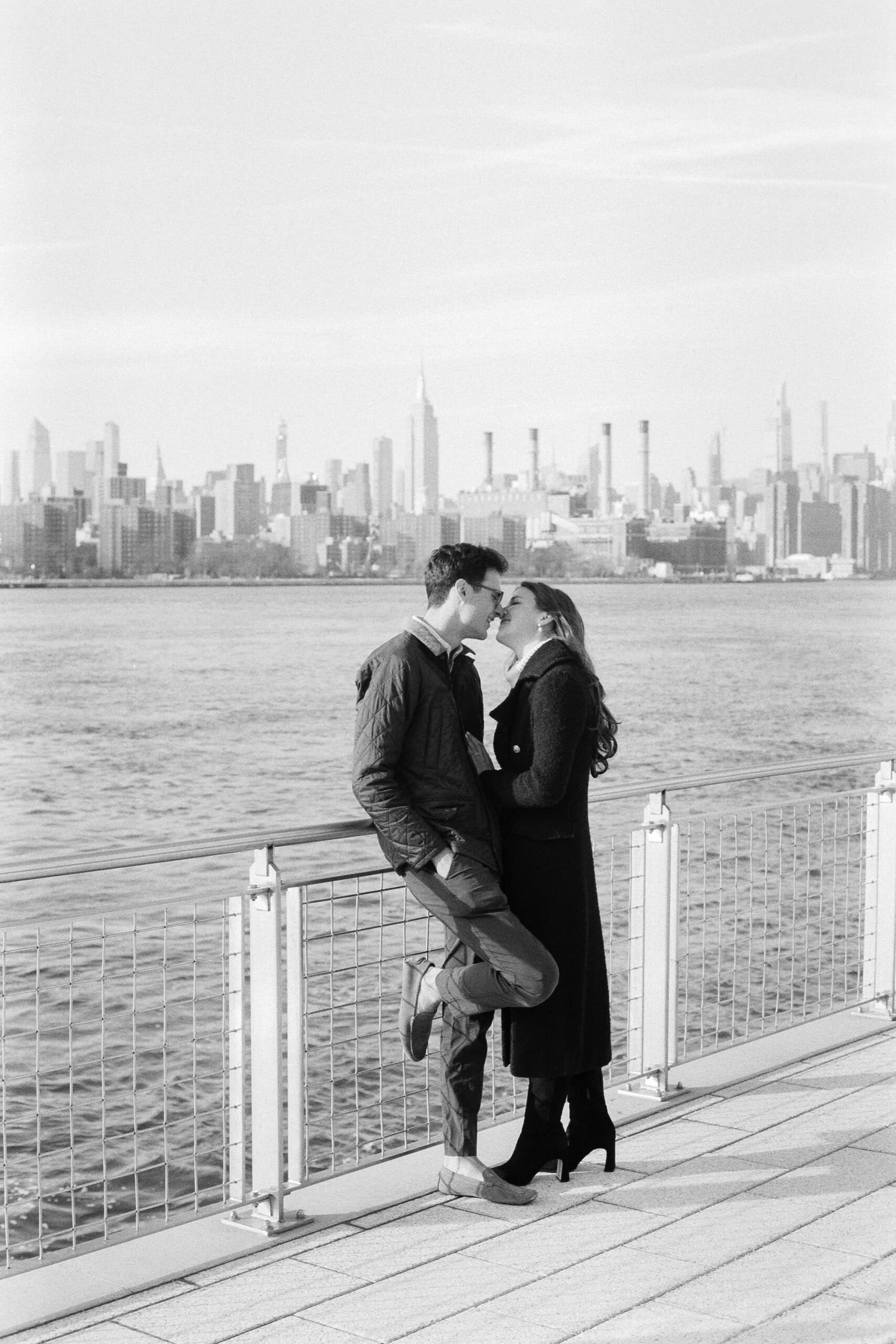 a man and woman kissing on a bridge by water