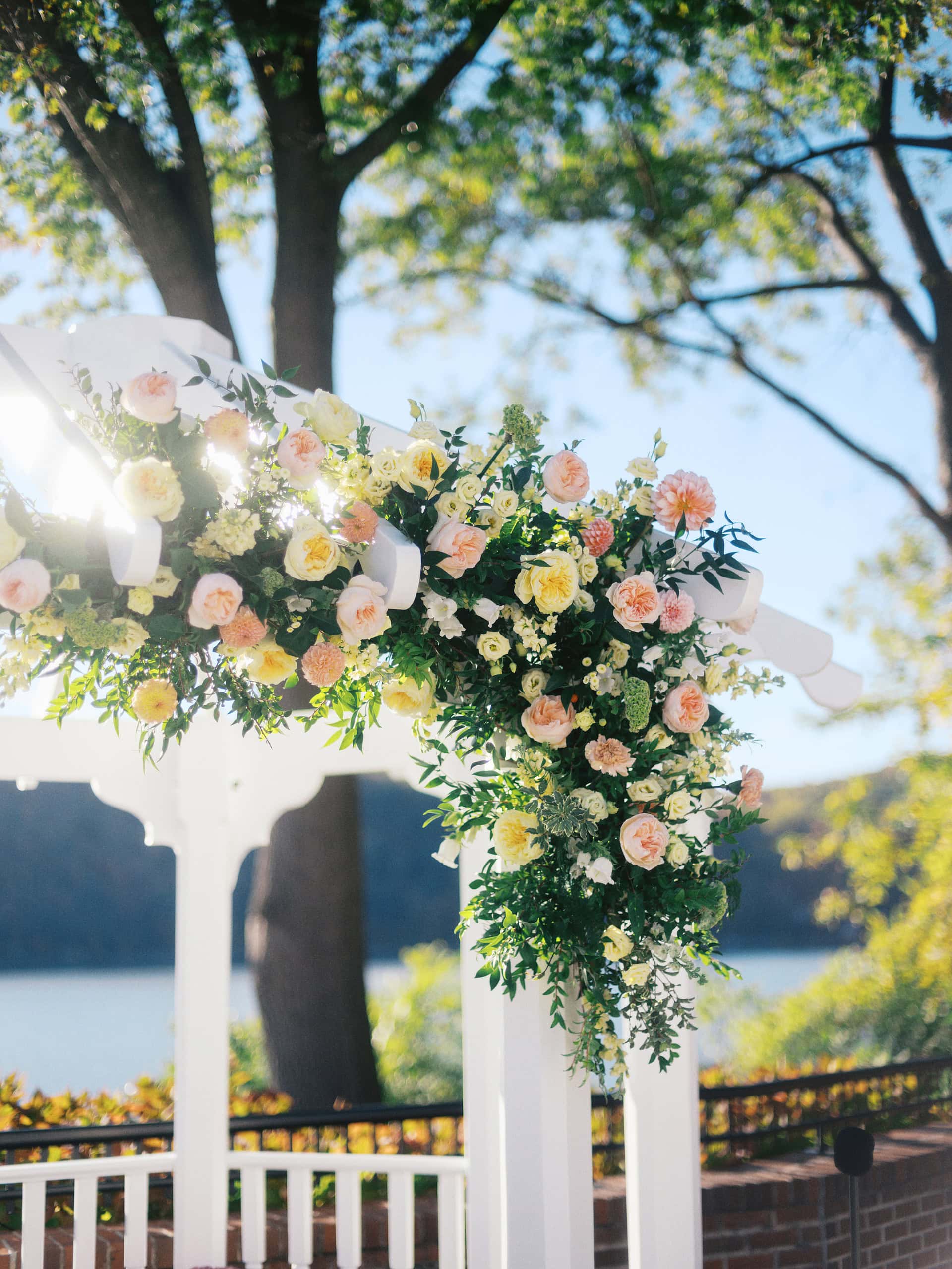 Wedding ceremony arch decorated with peach and yellow florals at The Grandview Poughkeepsie NY with Hudson River in the background